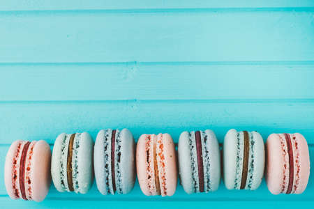 Line of sweet macaroons in pastel colors lie in a row on a turquoise wooden background, french almond cookie on a table, toning and copy spaceの写真素材