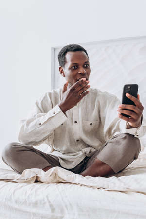 Smiling black man waves hand at videocall sitting on bedの写真素材