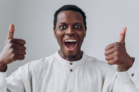 Emotional African-American guy shows thumbs up on light greyの写真素材
