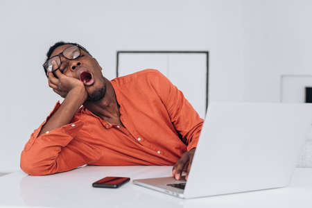 Tired African-American guy adjusts glasses at laptopの写真素材
