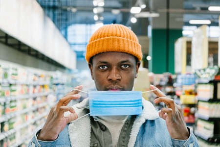 African-American man puts on blue disposable mask in storeの写真素材