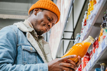 Thoughtful black man looks at bottle of juice in supermarketの写真素材