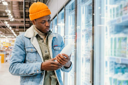 African-American guy takes milk from fridge in supermarketの写真素材