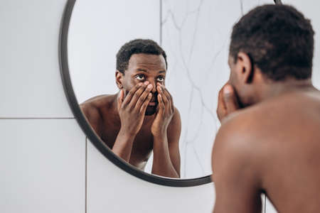 African-American man looks in mirror making face in bathroomの写真素材