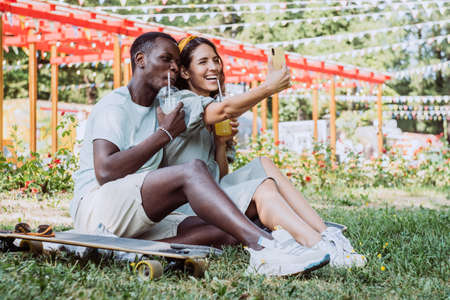 Afro-American man and white woman sit making selfie in parkの写真素材