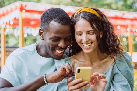 Afro-American man and young woman watch selfie on smartphoneの写真素材