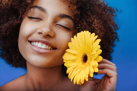 Mixed race young woman holds yellow flower and smilesの写真素材