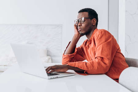 Tired African-American guy adjusts glasses at laptopの写真素材