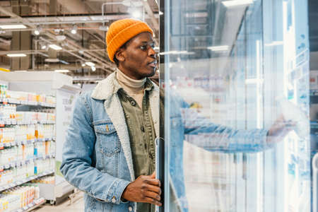 African-American guy takes milk from fridge in supermarketの写真素材