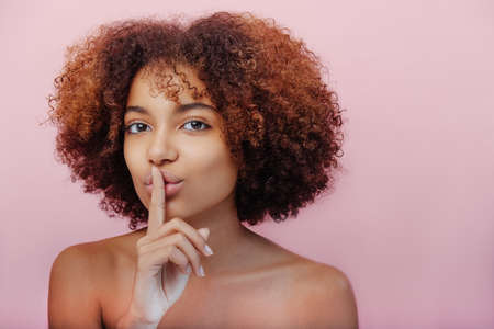 Mixed race young woman touches lips with forefingerの写真素材