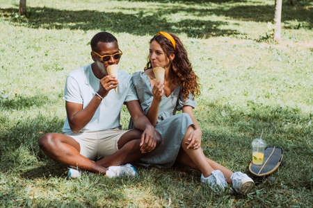 Black man and brunette young woman eat ice-cream on grassの写真素材