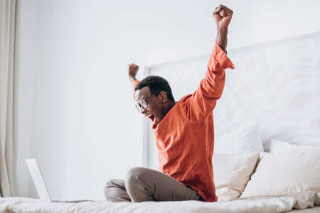 African-American guy puts hands up sitting near laptopの写真素材