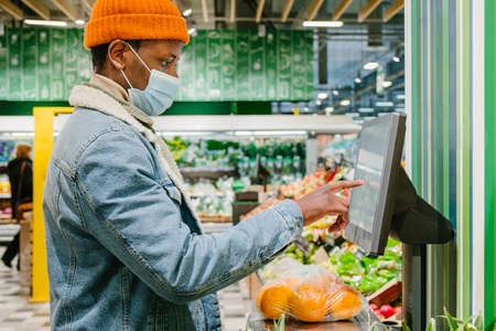 African-American guy in mask weighs oranges in supermarketの写真素材