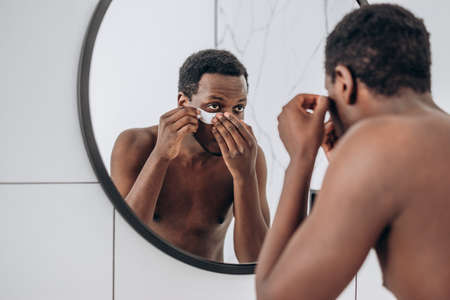 Handsome African-American guy uses eye patches in bathroomの写真素材