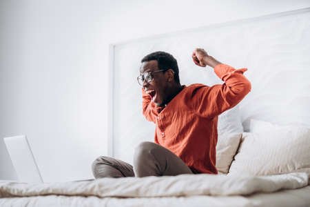 African-American guy puts hands up sitting near laptopの写真素材