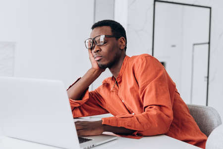 Tired African-American man sleeps leaning on hand at laptopの写真素材
