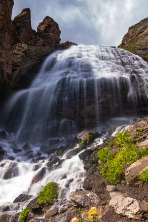 A majestic waterfall in the mountains, a mountain river falls from a high cliff onto stones on a sunny day, long exposureの写真素材