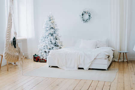 A bright spacious room with a large bed with white sheets and an elegant Christmas tree and a wreathの写真素材