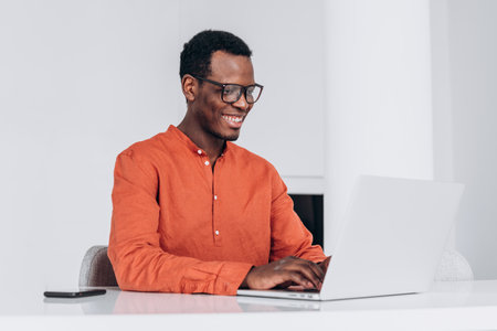 Young African-American guy works on modern laptop at tableの写真素材