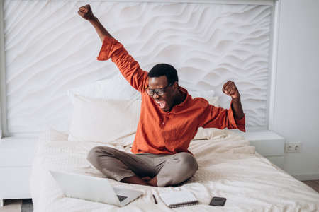 African-American guy puts hands up sitting near laptopの写真素材