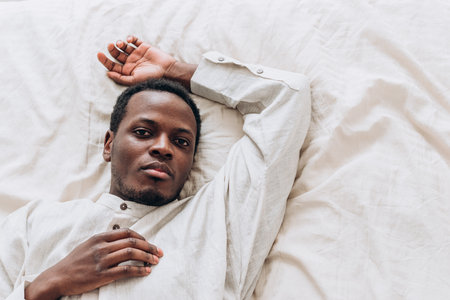 Calm African-American man in shirt sleeps on comfortable bedの写真素材