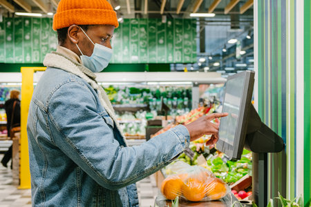 African-American guy in mask weighs oranges in supermarketの写真素材
