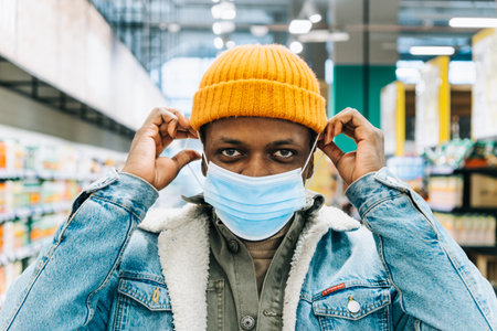 African-American man puts on blue disposable mask in storeの写真素材