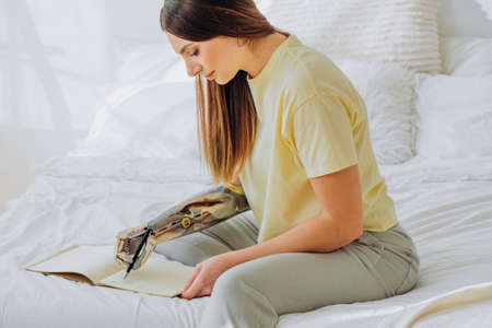 Woman writes in notebook with bionic arm sitting on bedの写真素材