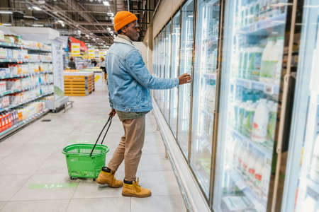 African-American guy with green basket walks along storeの写真素材
