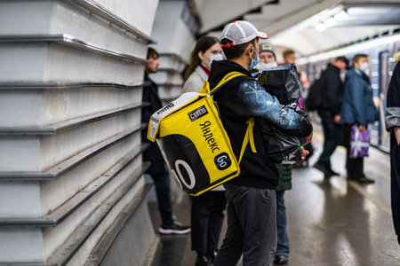 A Yandex delivery courier with a yellow bag is waiting for a train in the subway to deliver the...