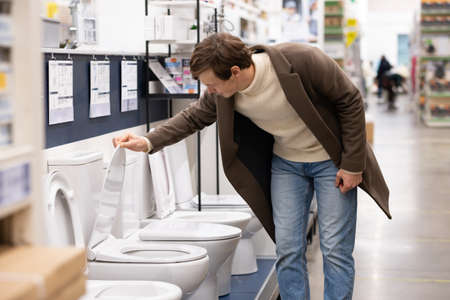 European man in a brown coat chooses a toilet in a construction supermarketの写真素材