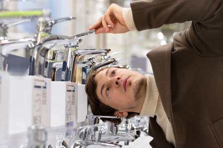 A young man carefully chooses a water mixer in a construction supermarketの写真素材