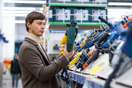 A young man chooses a hammer drill in a construction supermarket