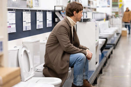 man in a coat is sitting on the toilet in a hardware storeの写真素材