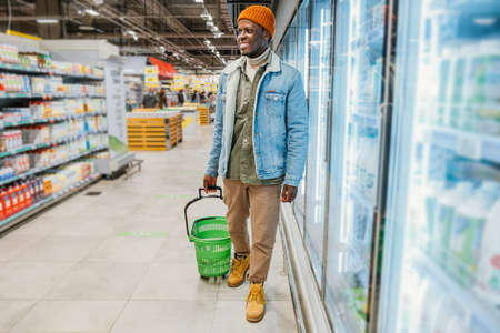 Black man with shopping basket stands in supermarketの写真素材