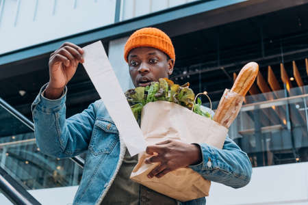 Doubting African-American man looks at receipt total in mallの写真素材