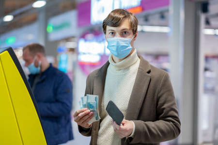 A young man in a medical mask took three thousand rubles from an ATM in a shopping centerの写真素材