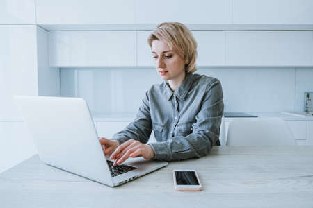 Business woman working at a laptop while sitting at a table in a bright officeの写真素材