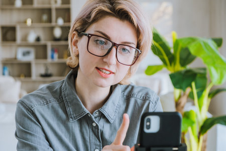 Woman blogger tells a lecture in front of the phone online in a cozy officeの写真素材