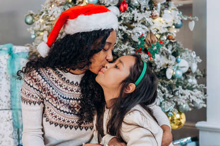 African American mom kisses child girl on cheek on Christmasの写真素材