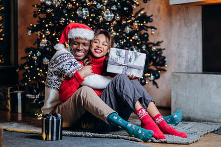 Woman and black man hug holding gifts near Christmas treeの写真素材