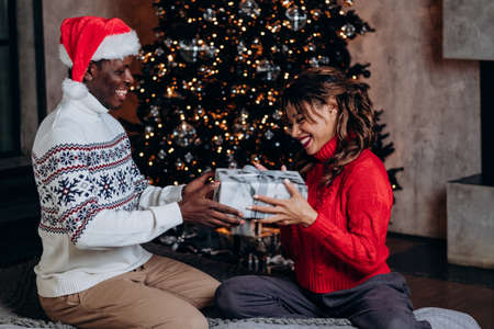 Black man presents girlfriend Christmas gift in festive moodの写真素材