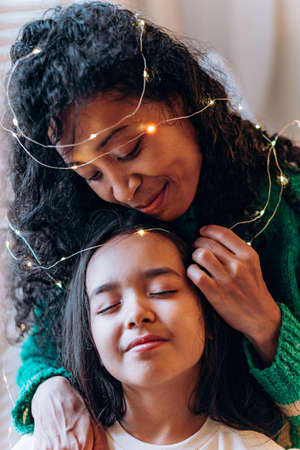 Girl and mother pose in garland against Christmas treeの写真素材