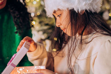 Brunette girl in Christmas hat opens festive presentsの写真素材