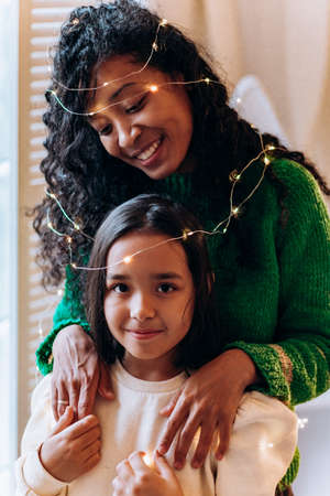 Girl and mother pose in garland against Christmas treeの写真素材