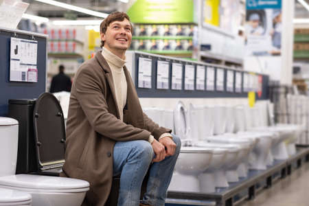 Man with brunet hair chooses toilet for apartment renovationの写真素材