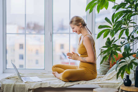 Athletic woman sits on windowsill and meditates at laptopの写真素材
