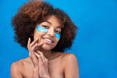 Curly-haired woman poses with smile and patches under eyesの写真素材