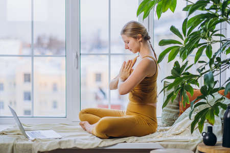 Young woman meditates sitting on windowsill at laptopの写真素材