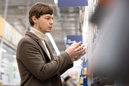 Brunet man with stubble looks for paint for renovationの写真素材